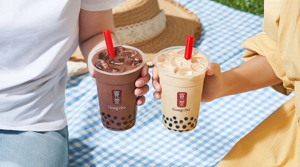 Couple holding Gong cha drinks at picnic