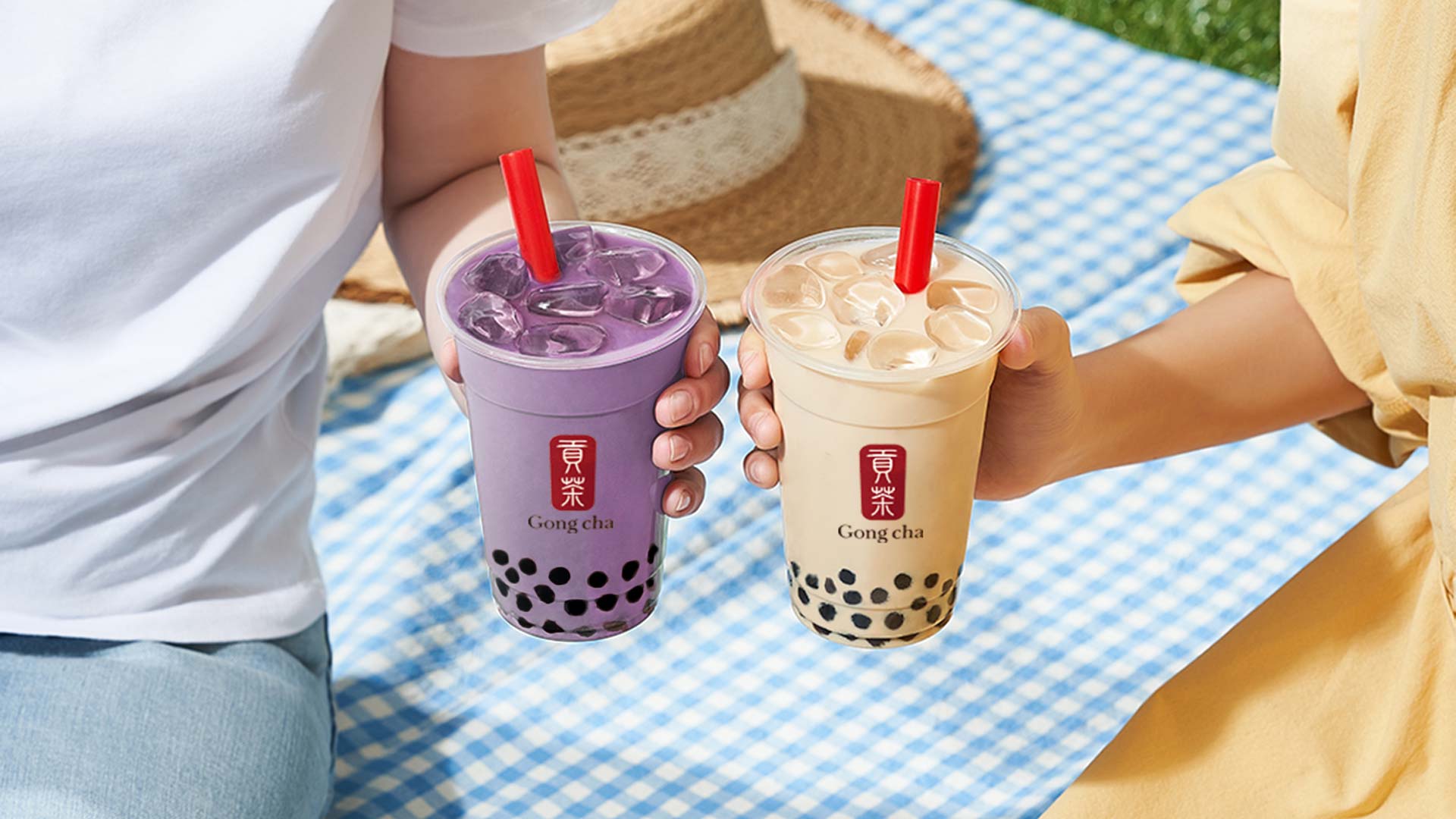 Couple holding Gong cha drinks at picnic